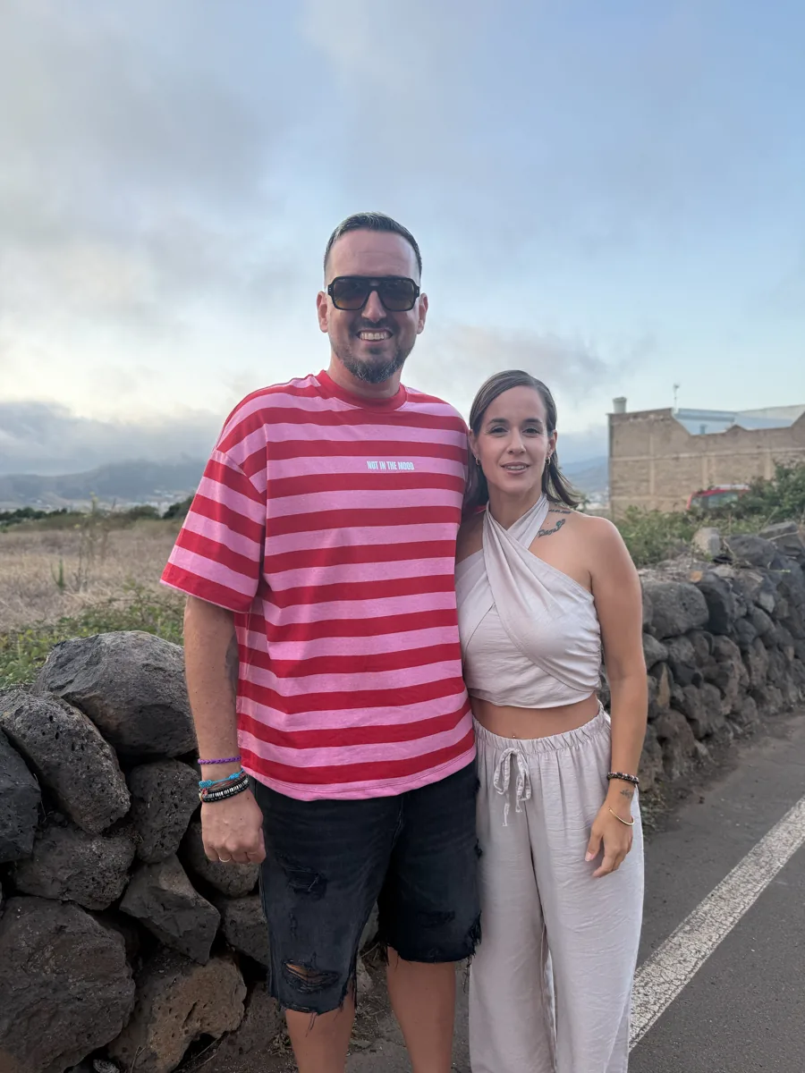 Jonay y Joana, sonrientes, junto a un muro de piedra